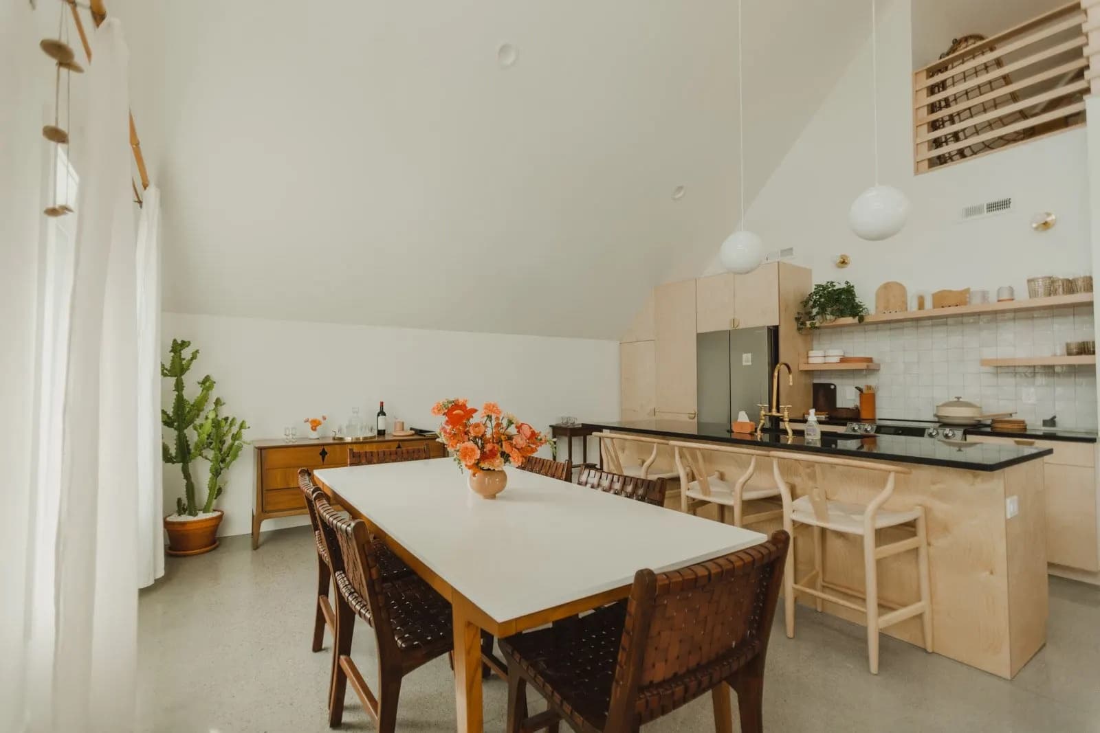 A bright kitchen and dining room under a vaulted ceiling, with light wood cabinets and a white dining table.